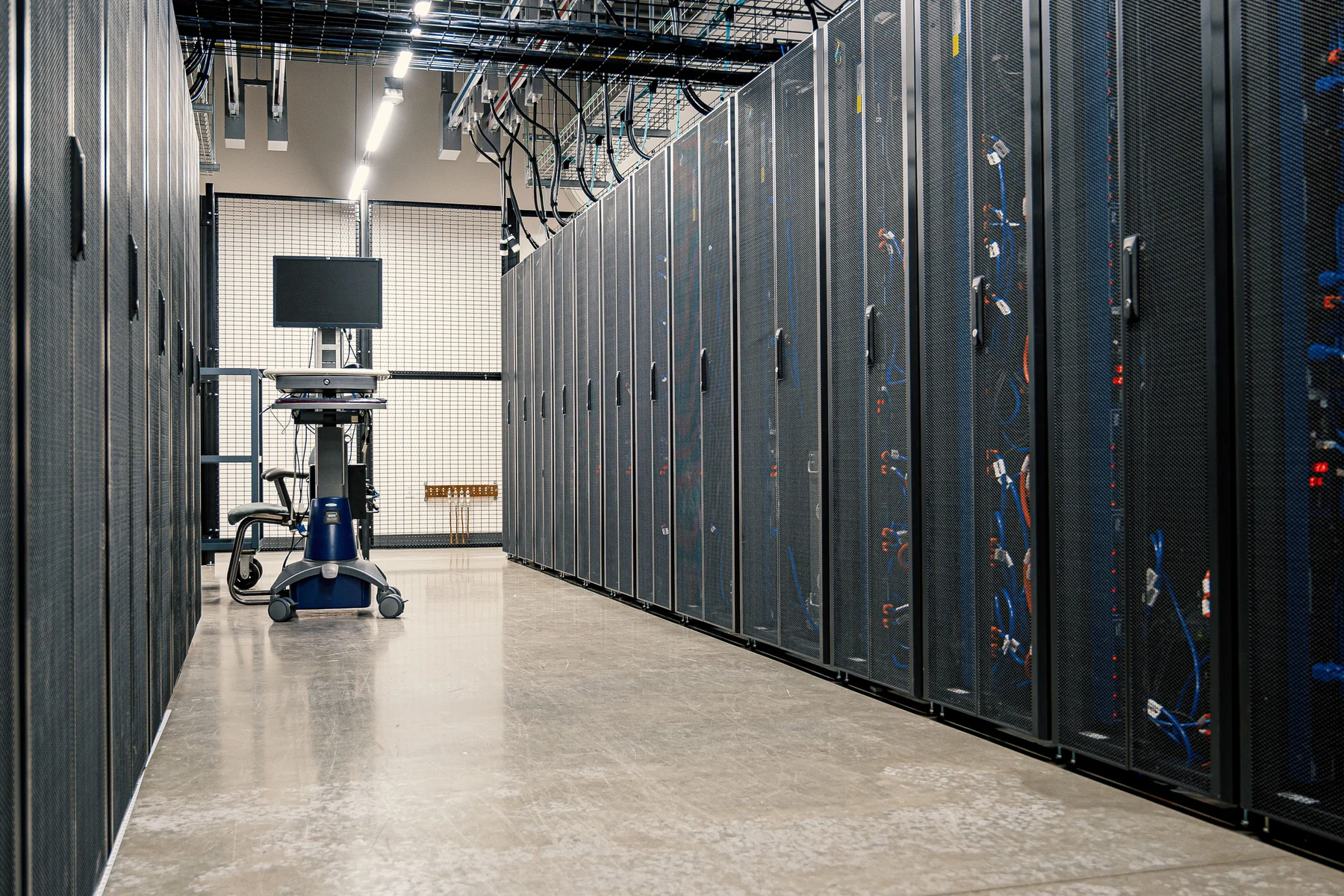 An aisle between rows of server cabinets and network equipment inside a data center.