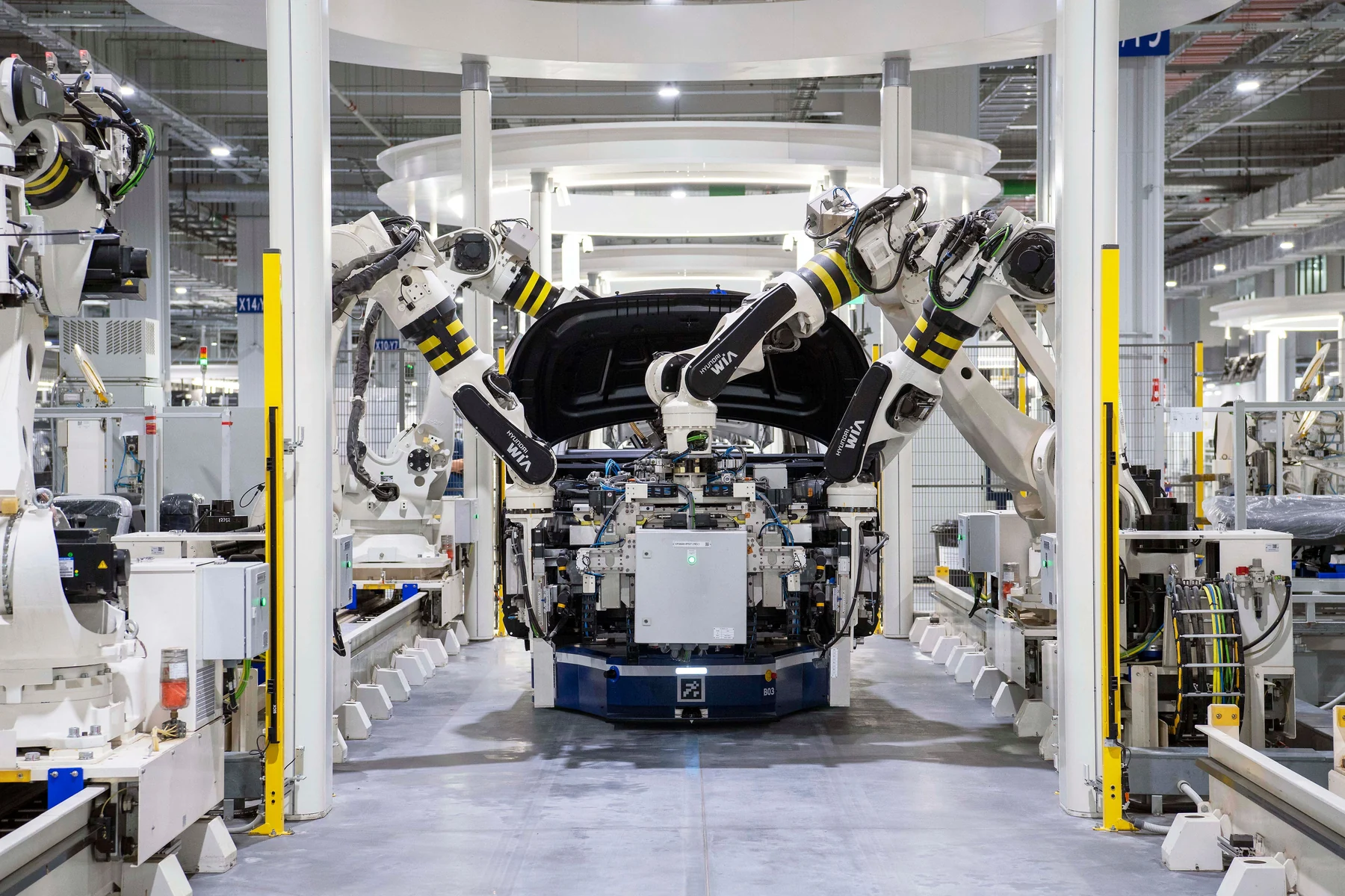 Robotic arms assembling a car inside a bright, modern manufacturing facility.