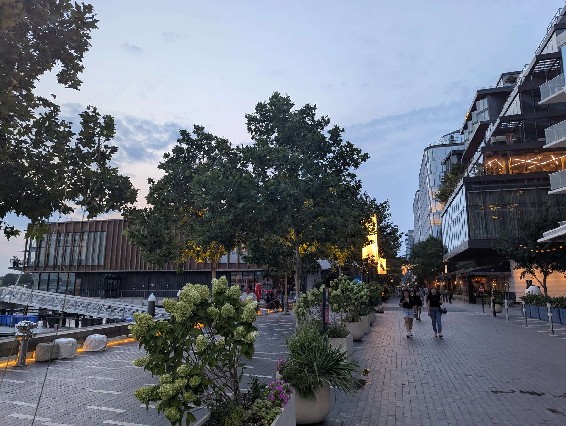 People walking beside restaurants and modern waterfront buildings on Wharf Street at dusk in Washington, D.C.